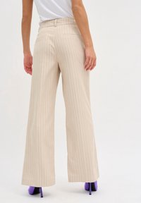 Béžové volné kalhoty s vertikálními pruhy, vysokým pasem, dvěma zadními kapsami a hladkou strukturou.