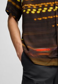 Short-sleeve shirt in dark fabric adorned with colorful abstract light patterns; features a subtle logo and a relaxed fit.