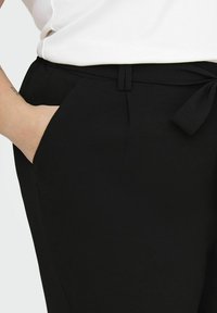 Pantalones negros hechos de una tela texturizada, con un bolsillo frontal, un detalle de cinturón de lazo y una cinturilla suave.
