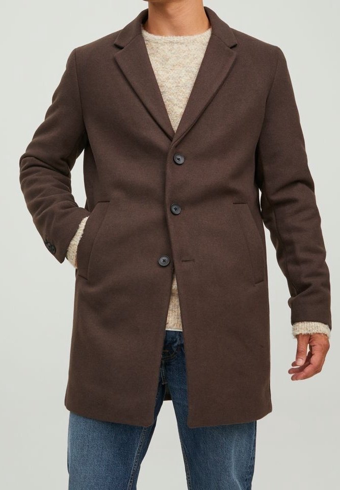 Cappotto in misto lana marrone con colletto a lancia, bottoni monopetto, tasche laterali e linea dritta, indossato sopra un maglione leggero e jeans.
