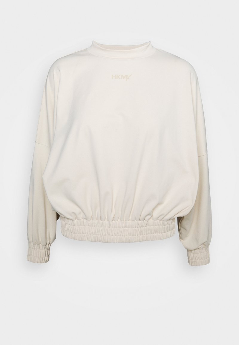 Sweat-shirt à manches longues couleur crème avec taille et poignets élastiqués, col montant, et logo discret centré près de l'encolure.
