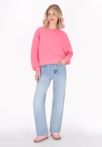Sudadera rosa de gran tamaño con mangas largas, combinada con jeans rectos azul claros y zapatos rosas. Conjunto casual moderno.