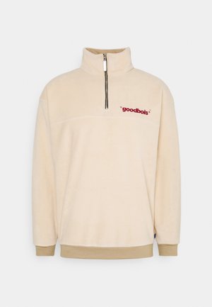 Pile beige con collo alto, chiusura a mezza cerniera e testo ricamato bordeaux "goodbois" sul petto. Polsini e orlo a costine.