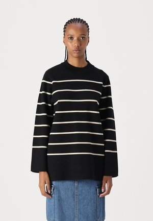Schwarz- und cremefarbener gestreifter Pullover mit langen Ärmeln und geripptem Rundhalsausschnitt, aus weichem Material, getragen mit einem Jeansrock.