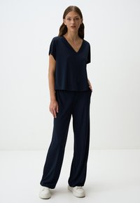 Haut bleu marine à manches courtes et encolure en V associé à un pantalon large de la même couleur. Tissu lisse et léger avec une coupe décontractée. Baskets blanches.