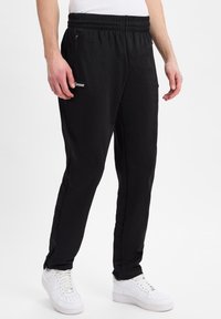 Schwarze Sporthosen mit einer Kordelzugtaille, Reißverschlusstaschen an den Seiten und dezentem Branding. Hergestellt aus einem weichen, elastischen Stoff.