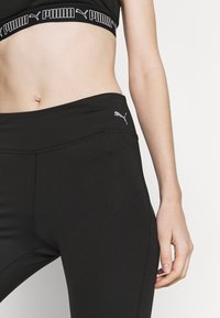 Czarne legginsy sportowe z wysokim stanem, z szarym logo Pumy na biodrze i gładkim, elastycznym materiałem.