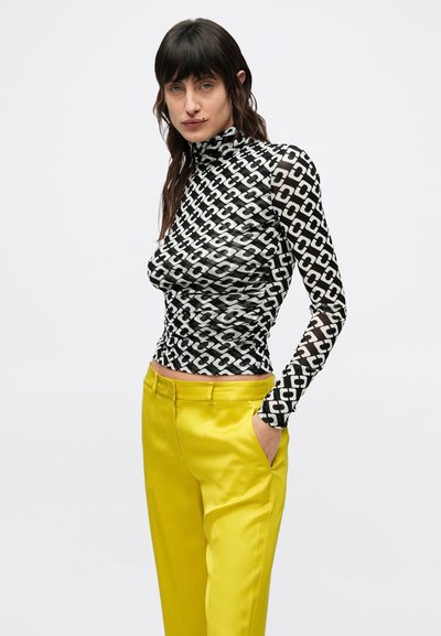 Langarm coltrui in zwart-wit kettingpatroon, gecombineerd met felgele satijnen broek met steekzakken aan de voorkant en een aangesloten pasvorm.