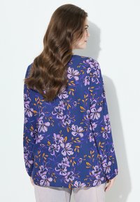 Blusa a maniche lunghe floreale in blu navy con motivi di fiori viola e arancioni; presenta una vestibilità ampia e un tessuto morbido e testurizzato.