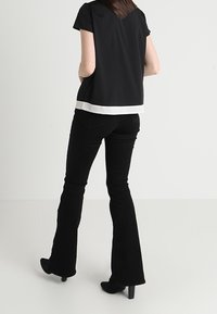 Top corto nero a maniche corte con orlo bianco, abbinato a pantaloni neri a palazzo. Il tessuto è liscio, con una vestibilità casual e un design semplice; senza motivi o dettagli.