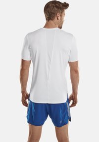 Weißes Sportshirt mit kurzen Ärmeln, mit einem Netzpaneel auf der Rückseite, kombiniert mit blauen Shorts. Glatte Textur und atmungsaktives Design.