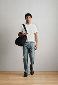 Biele tričko, svetlomodré rifľové nohavice, čierna kabelka na rameno a čierne topánky. Jednotlivec kráča po drevenej podlahe s jednoduchým pozadím.