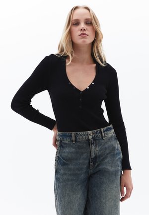 Black ribbed long-sleeve top with a V-neckline, featuring three button accents. Worn with high-waisted faded blue jeans.