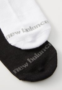 White and black socks are laid next to each other, each featuring "new balance" text in gray near the top.
