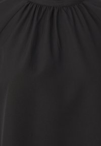 Tela negra con una textura suave y ligero brillo. Presenta detalles fruncidos en el escote, creando una silueta suave y fluida.