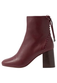 Botín de piel burdeos con punta afilada, superficie texturizada, tacón de madera apilada y detalle de cordones decorativos en el lateral.
