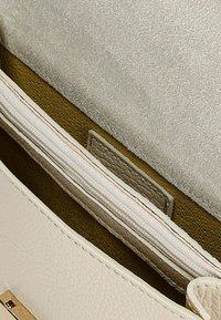 Interiér béžové kožené kabelky s jemně zelenou podšívkou. Obsahuje kapsu na zip a akcent z texturované semiše. Jemné švy.