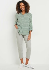 Camicia button-up verde chiaro con pois bianchi, abbinata a pantaloni cropped grigi chiari e sneakers bianche. Vestibilità rilassata e stile casual.