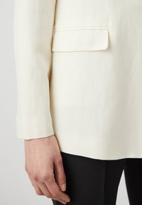 White tailored blazer fabric, smooth texture, single pocket detail, paired with black fitted trousers, showcasing clean lines and professional style.