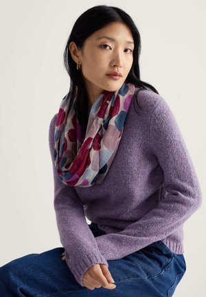 Purpursarkana adīta džemperis ar garām piedurknēm, kombinēts ar daudzkrāsainu, rakstainu nebeidzamu šalli ar ziedu formām sarkanā, zilā un rozā krāsā.