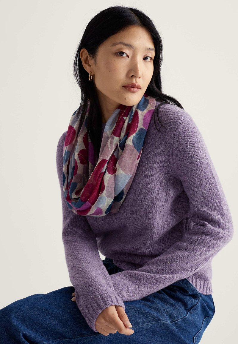 Lilla kootud kampsun pikkade varrukatega, millele on lisatud mitmevärviline mustriga lõpmatussall, kus on punased, sinised ja roosad lillemotiivid.