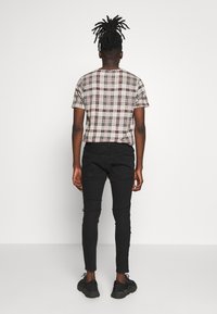 Camisa de cuadros de manga corta en tonos beige, negro y rojo, combinada con jeans ajustados negros y zapatillas negras, vista desde la espalda.