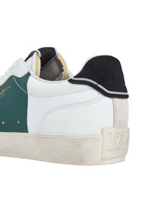 Sneaker with white leather, green panel, and textured black suede heel tab. Features a beige rubber sole and embossed logo detail.
