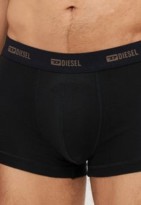 Crni pamučni bokserice s kontrastnim tamnosivim elastičnim pojasom na kojem se nalazi naziv brenda "DIESEL" u smeškastom slovu.