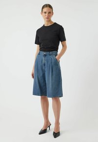 Mustapaitainen puuvillapaita, joka on yhdistetty sinisiin farkkuculotteihin, joissa on laskokset ja sivutaskut, asusteena mustat teräväkärkiset korot.