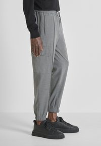 Grijze afgezette broeken met een elastische tailleband, zijzakken en elastische boorden, gecombineerd met zwarte sneakers met ribbelzolen.