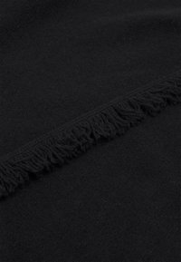 Tissu noir doux plié avec un détail de bordure à franges visible le long de la ligne de pli.