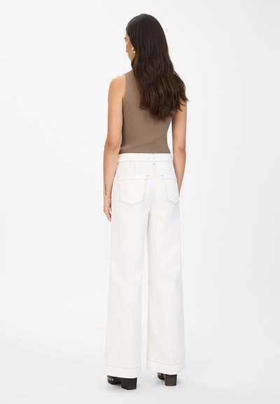 Brun ribbestrikket tanktop paret med høyhalsede, vide hvite jeans. Jeansene har kontraststing og baklommer.