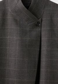 Veste en laine gris foncé avec un motif à carreaux subtil et un seul bouton noir visible près du col.