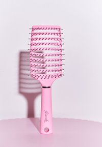 Brosse à cheveux rose avec une large tête rectangulaire, un design aéré, des poils en métal et un manche texturé avec un trou pour l'accrocher.