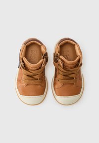 Brązowe skórzane buty typu high-top z białymi gumowymi podeszwami, z sznurówkami i zamkiem błyskawicznym z boku, teksturowanymi akcentami ze skóry oraz logo marki.