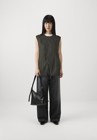 Mörkgrön ärmlös topp med vita ränder, kombinerad med vida mörk denimbyxor. Modellen håller en svart läderhandväska.