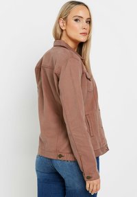 Veste en denim marron avec un col, poches avant et détails en bouton. Le matériau est texturé et le design est ajusté avec des manches longues.
