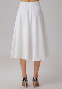 Jupe blanche en A, de longueur genou, avec une texture lisse et une fermeture éclair à l'arrière, accompagnée de chaussures à talons hauts métalliques.