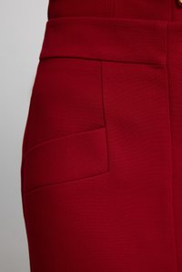Pantalon rouge en tissu texturé avec une taille plate, des poches latérales et des coutures nettes pour un look soigné.