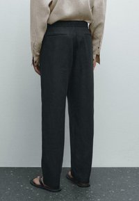 Black linen trousers with a relaxed fit, featuring two back pockets and a smooth texture. Worn with brown flip-flops.