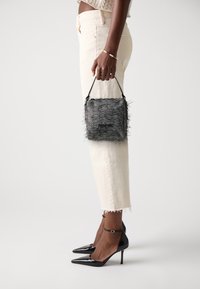 Sac à main en noir et blanc en chevrons avec une frange texturée, une courte poignée et une forme rectangulaire compacte. Associé à un jean court de couleur claire et des talons.