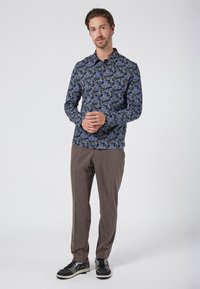 Langsleeve shirt met een blauw bloemenpatroon op een zwarte achtergrond, gecombineerd met bruine gestructureerde broek en zwarte sportschoenen met witte accenten.