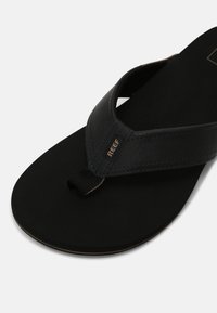Black leather flip-flop with textured straps, fabric lining, and a soft black footbed. Features a woven logo detail on the strap.