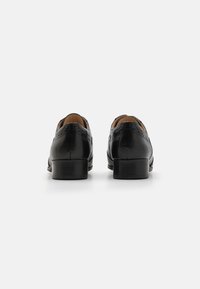 Scarpe eleganti in pelle nera con finitura liscia, dotate di dettagli decorativi brogue e tacco impilato. Design semplice e classico.
