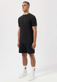 Svart kortärmad T-shirt med logotryck, i kombination med svarta shorts. Vita sneakers och strumpor ingår. Minimal design och avslappnad passform.