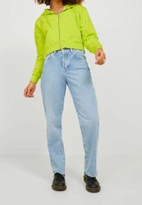 Limetkově zelená zkrácená mikina s zipem, v kombinaci se světle modrými rovnými džíny. Černé boty dotvářejí outfit. Jednoduchý design a ležérní styl.