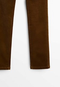 Parties basses des jambes d’un pantalon en velours côtelé marron avec des ourlets droits sur fond blanc.