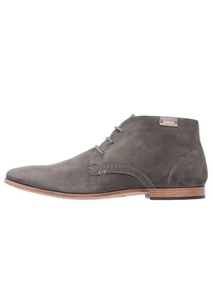 Bottines en suède gris avec un bout pointu, trois œillets, des accents de couture clairs et une semelle en bois marron contrastante.