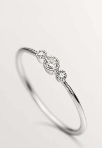 Anillo de plata que presenta tres piedras preciosas claras de diferentes tamaños, engastadas con garras en forma circular, con una banda suave y pulida y un diseño minimalista.