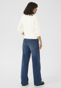 Pull en maille blanc à manches trois-quarts, associé à un jean en denim bleu taille haute et large, avec des poches arrière et un délavage clair.